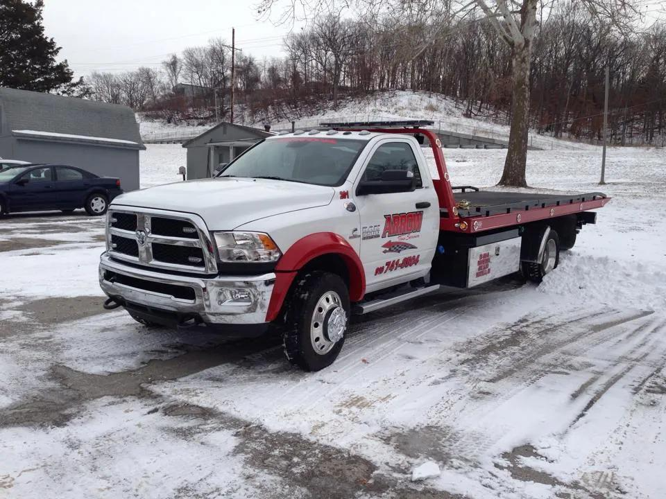 White and red tow truck parked on snow-covered ground in front of a building.