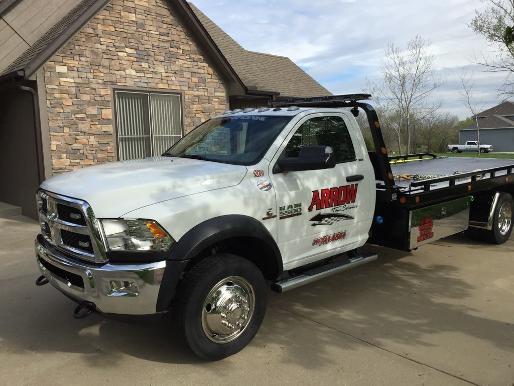 White Arrow towing truck parked in a driveway in front of a brick building.