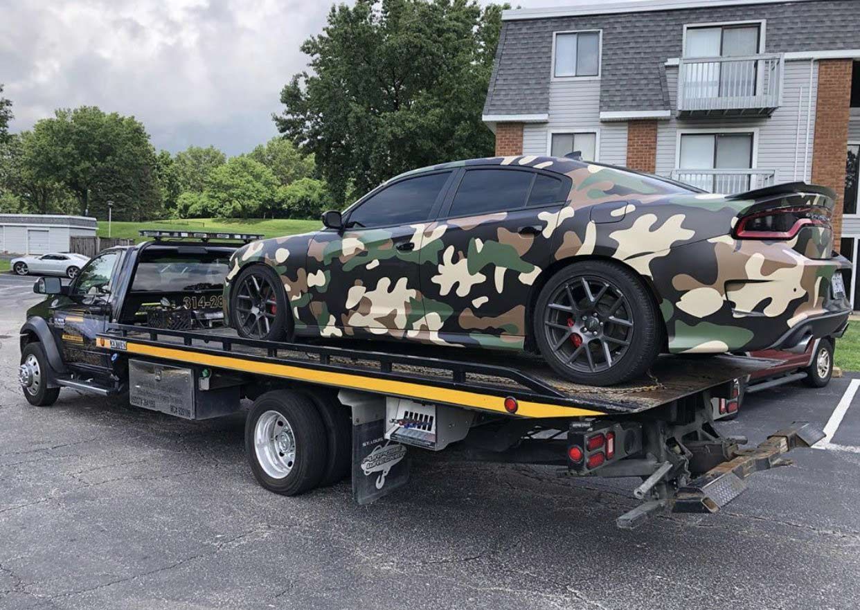 A camouflage car is being towed by a tow truck.
