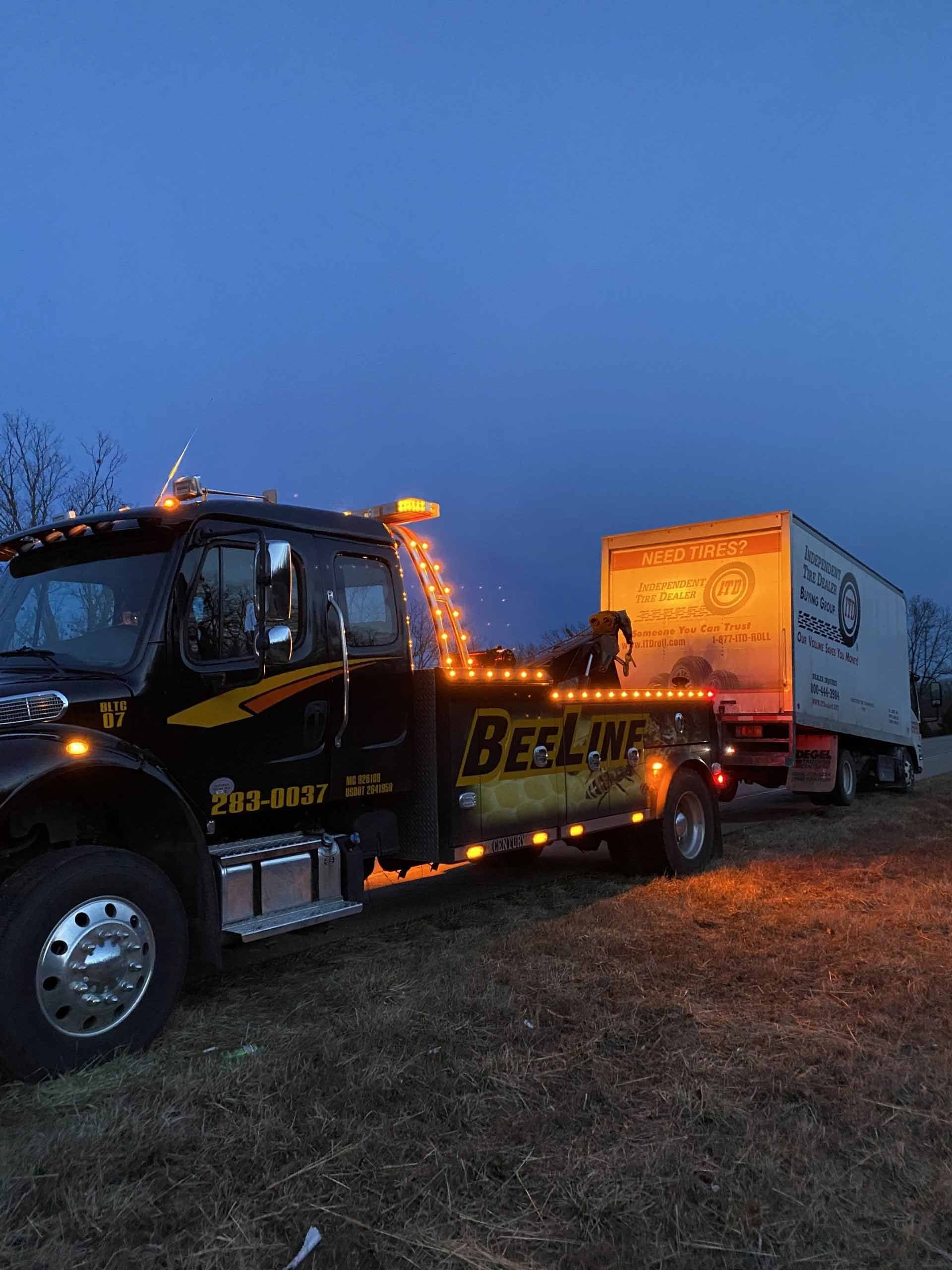 A tow truck is towing a semi truck in a field at night.