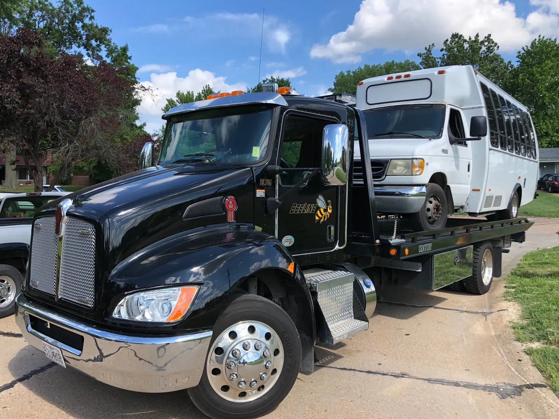 A black tow truck is carrying a white bus on the back of it.