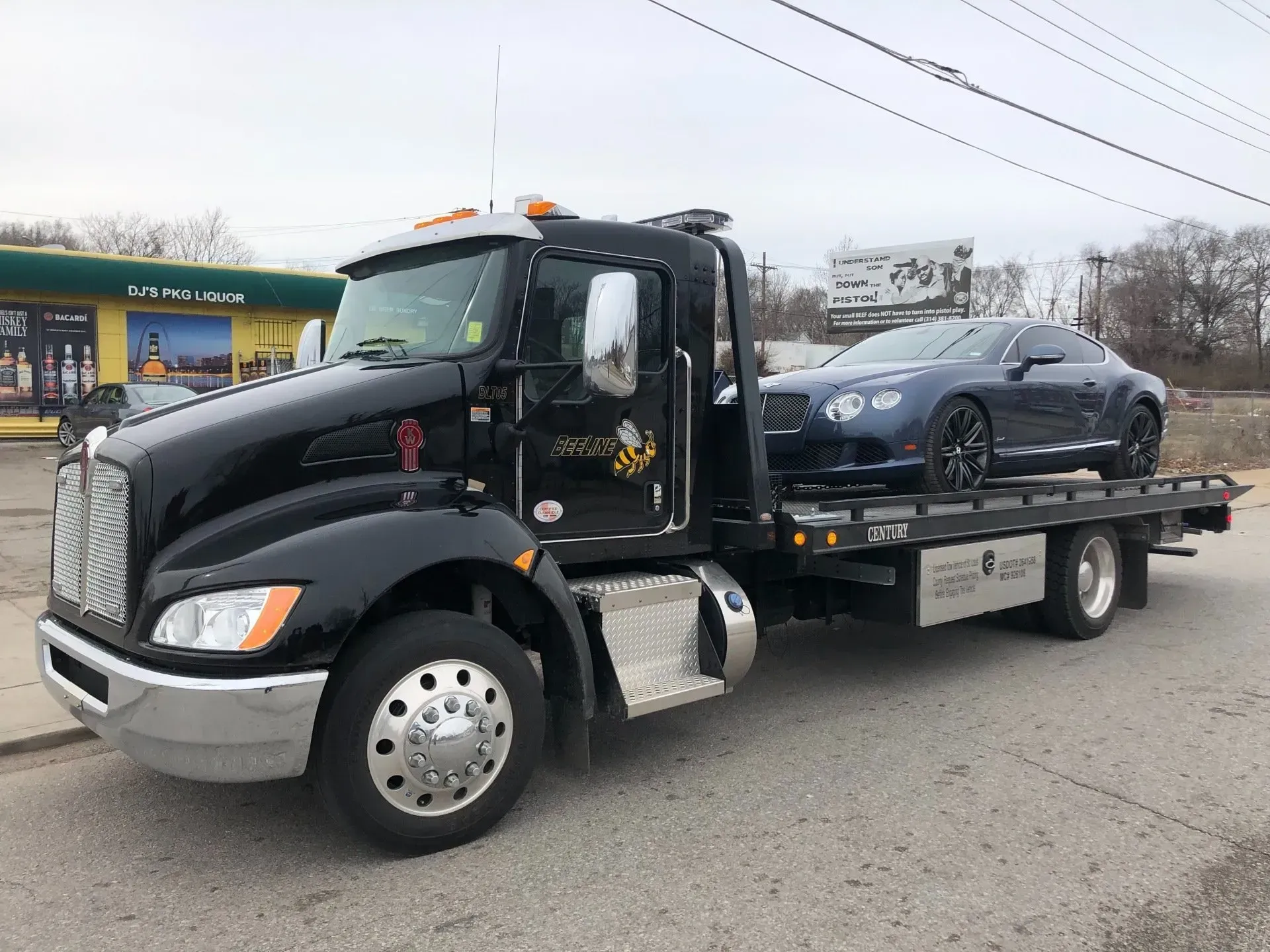A black tow truck is carrying a bentley on the back of it.