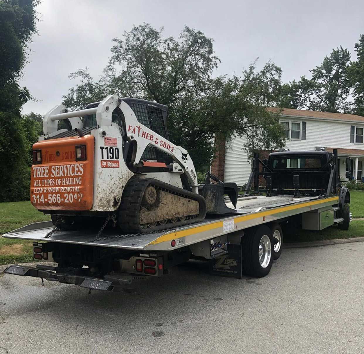 A tow truck with a bobcat on the back of it