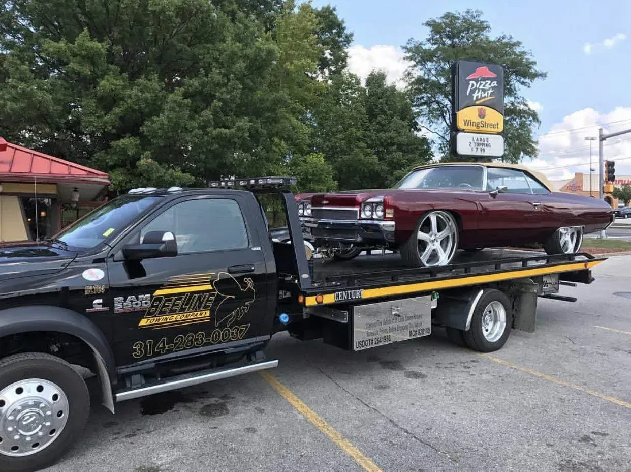 A tow truck is towing a red car in a parking lot.