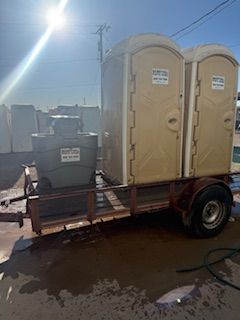Two portable toilets and a water tank on a trailer, outside on a sunny day.