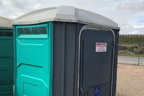 Two portable toilets are sitting next to each other in a gravel lot.