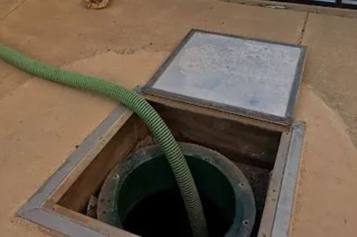 A green hose is being pumped into a septic tank.