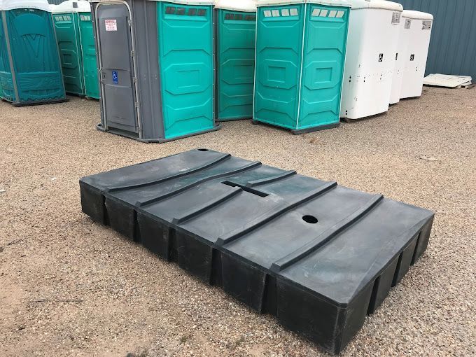 A black container is sitting in front of a row of portable toilets.