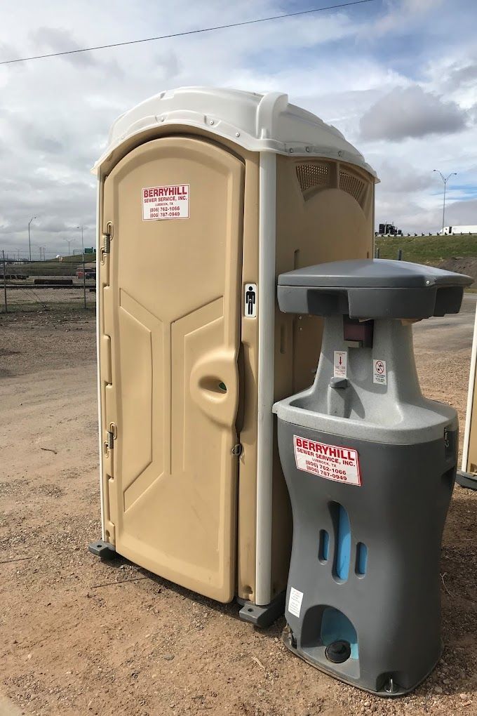 A portable toilet and a hand sink are sitting next to each other on a dirt road.