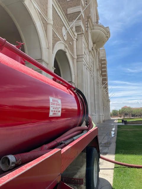 A red tank with a hose attached to it is parked in front of a building.