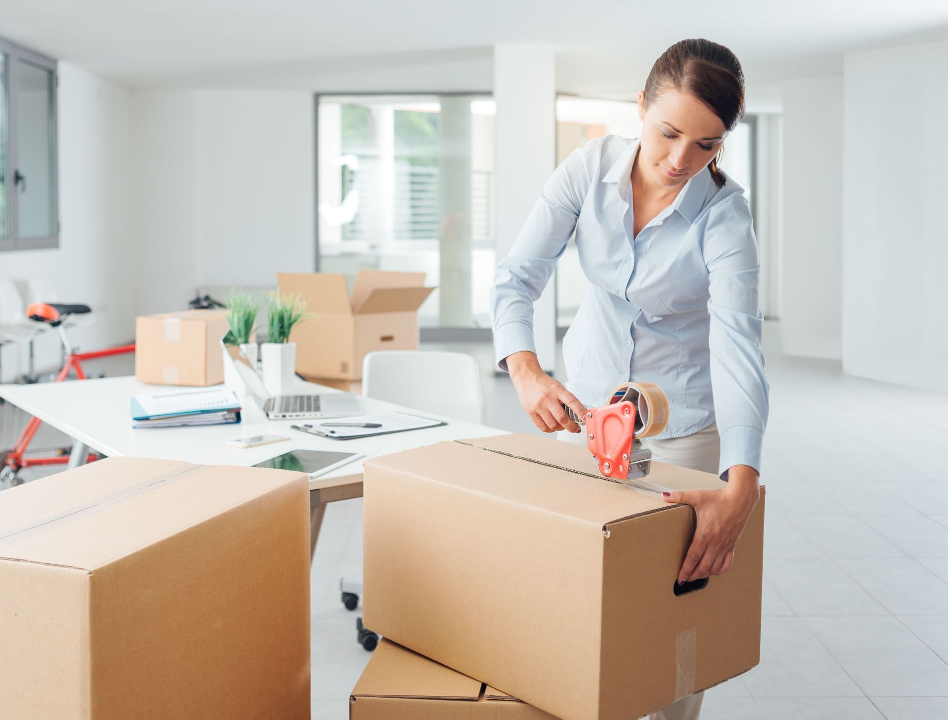 Person sealing cardboard boxes in a bright, empty office moving setup