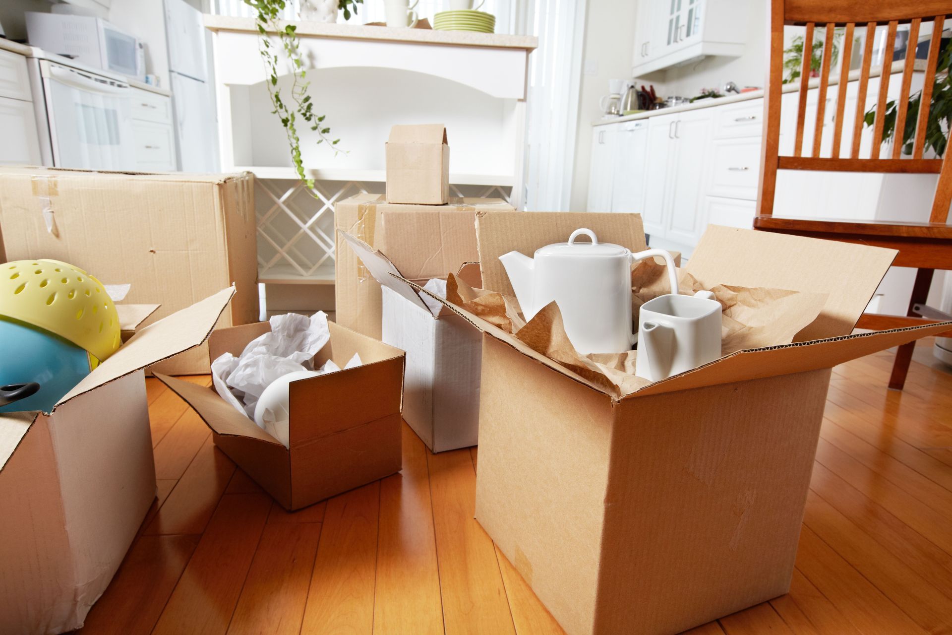 Packed moving boxes and kitchen items scattered across a bright wooden-floored room