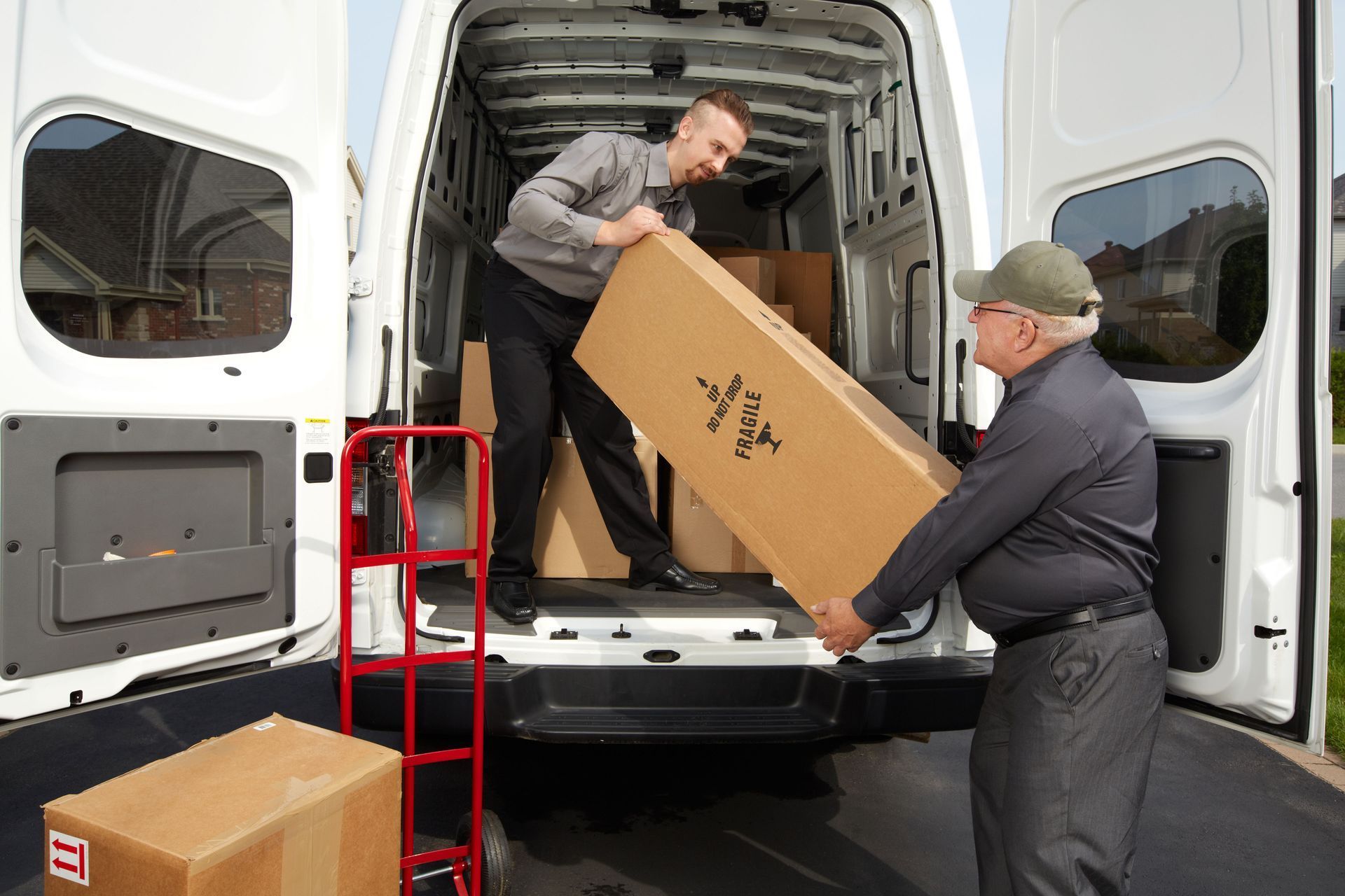 Two men loading a large cardboard box into a white delivery van at the rear