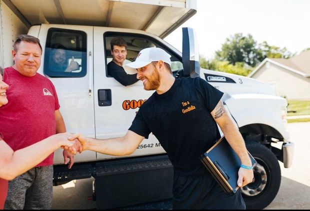 Three people shake hands beside a white truck on a sunny street.