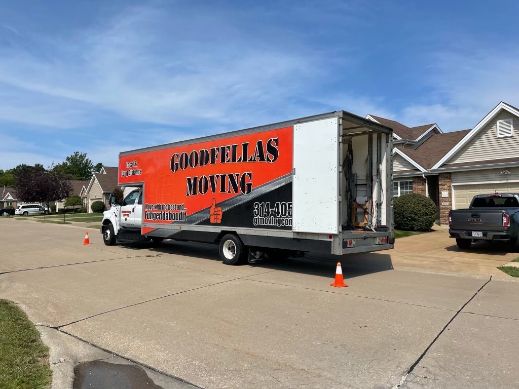 Moving truck parked in a suburban driveway with orange signage and traffic cones.