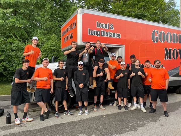 Group of people in orange and black posing beside a red Goodwill long-distance truck outdoors.