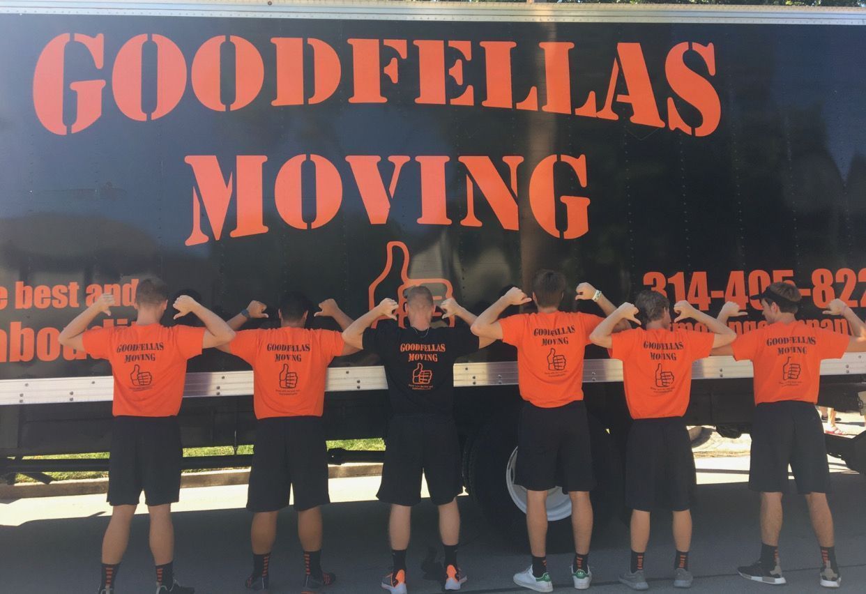 Goodfellas Moving team posing in orange shirts in front of a truck logo backdrop