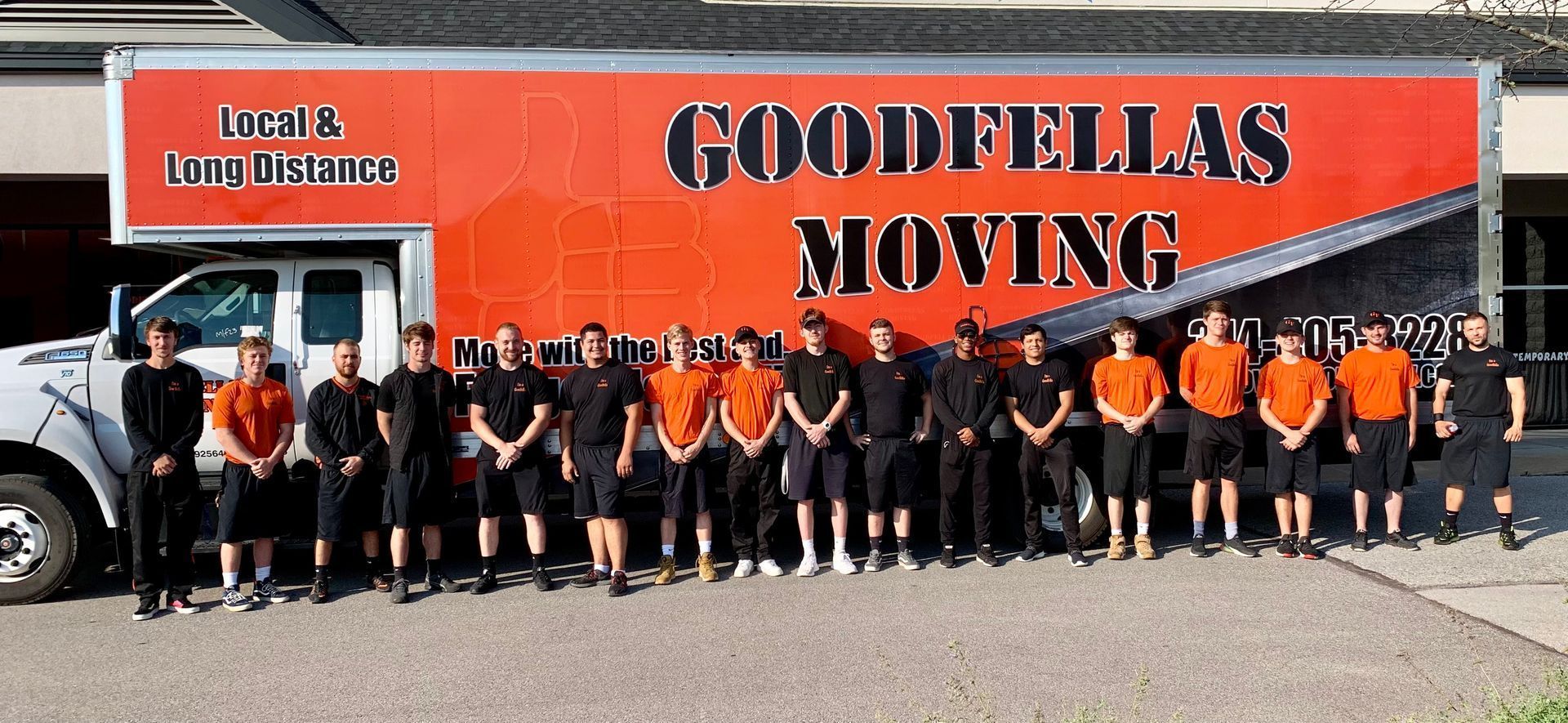 Goodfellas Moving crew posing in front of an orange moving truck with a white tow truck beside it