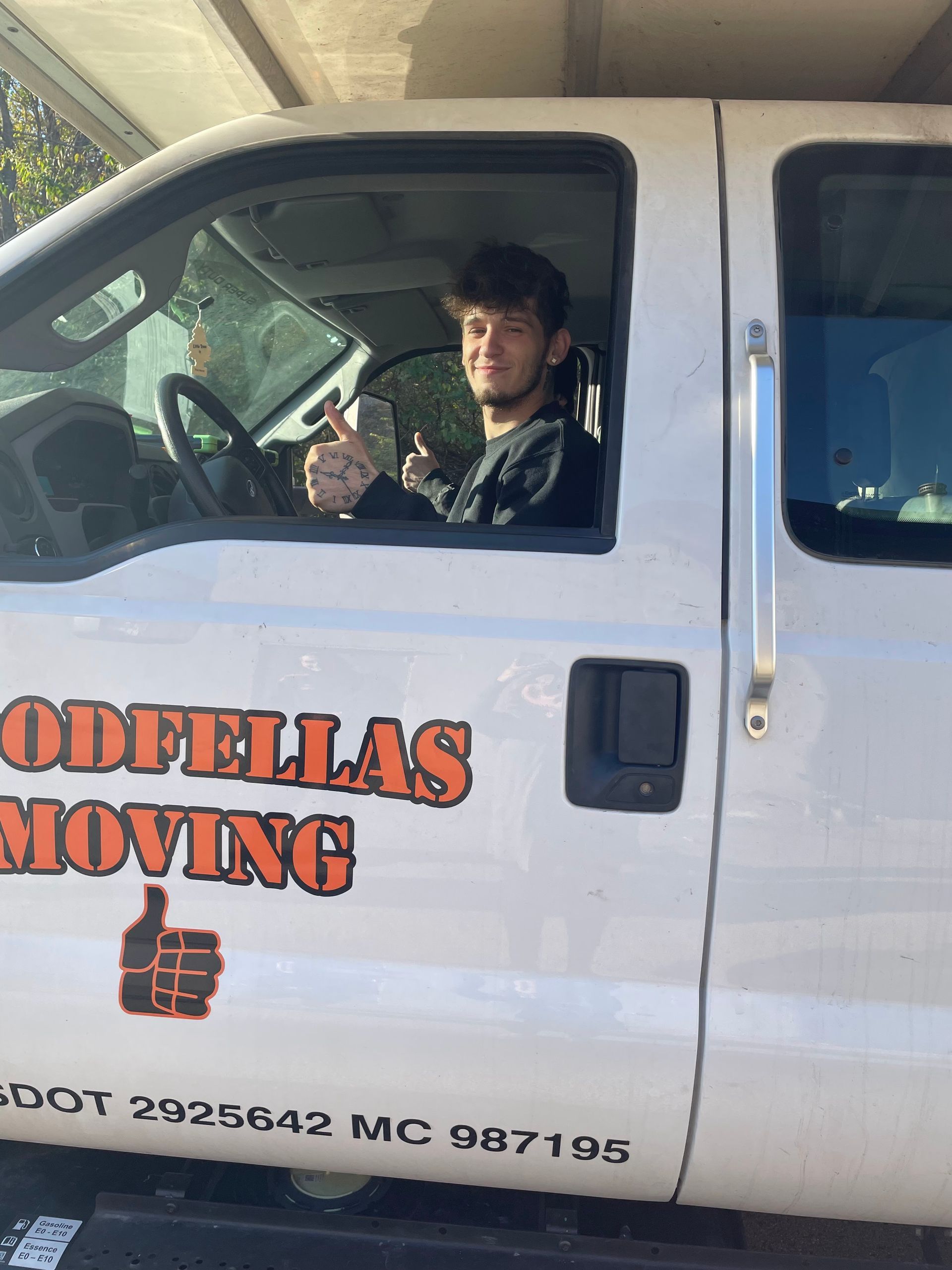 Mover in a white truck labeled “DODGELLAS MOVING,” holding up a hand inside the cab.