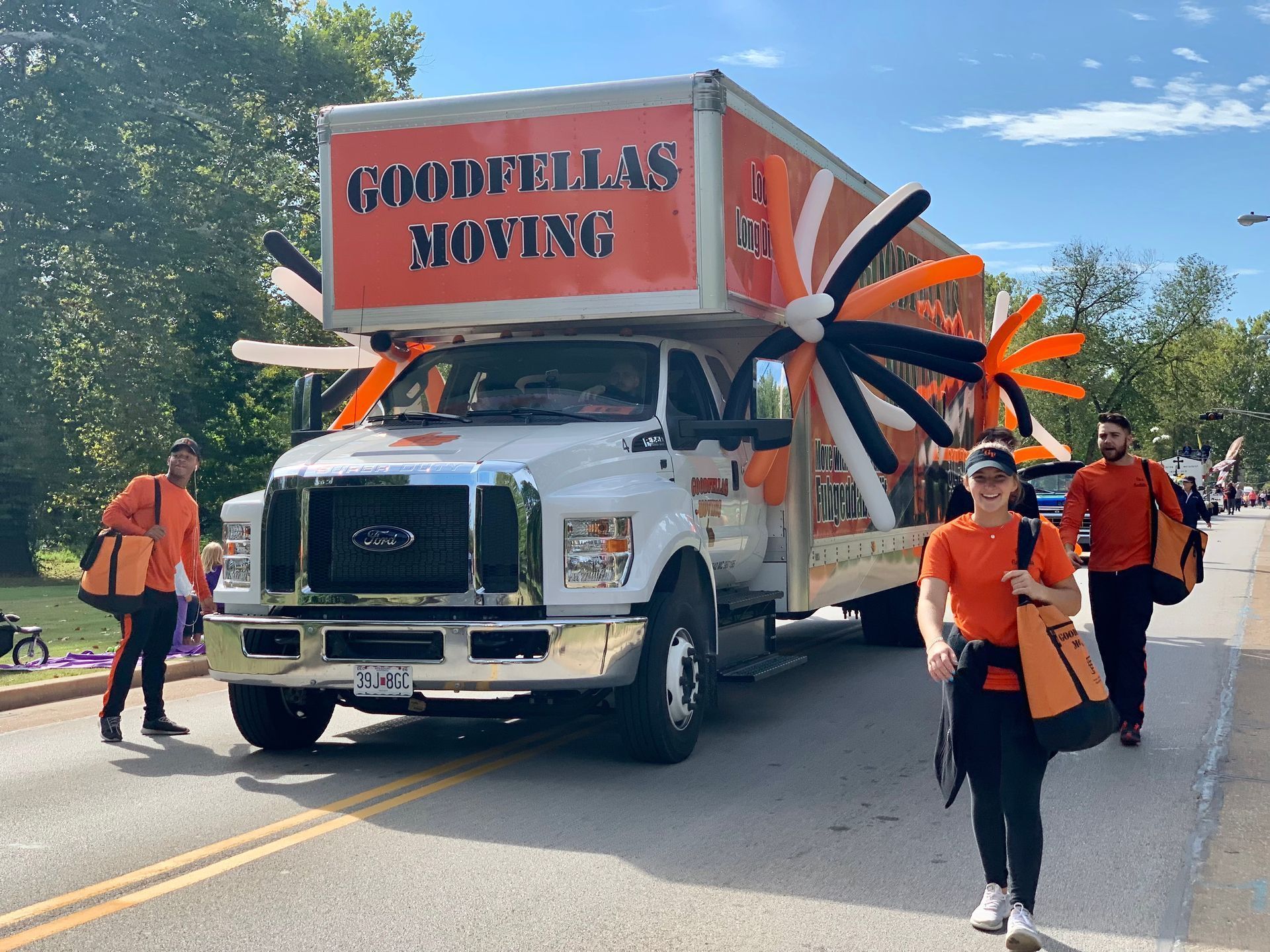 Moving truck with movers on a sunny street, orange logo, carrying a large inflatable slide and supplies