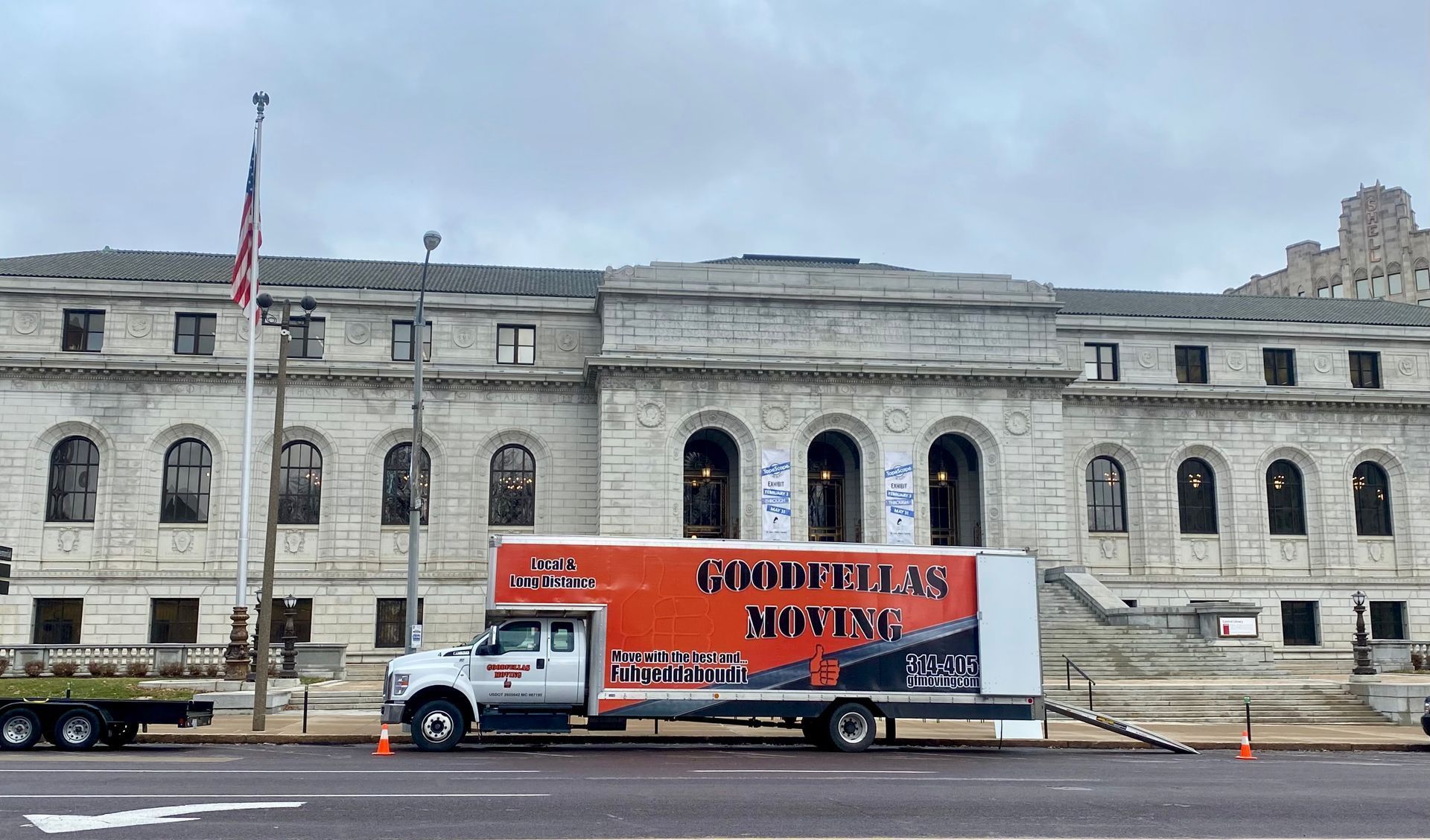 White box truck with red graphics parked in front of a large stone building and flagpole.
