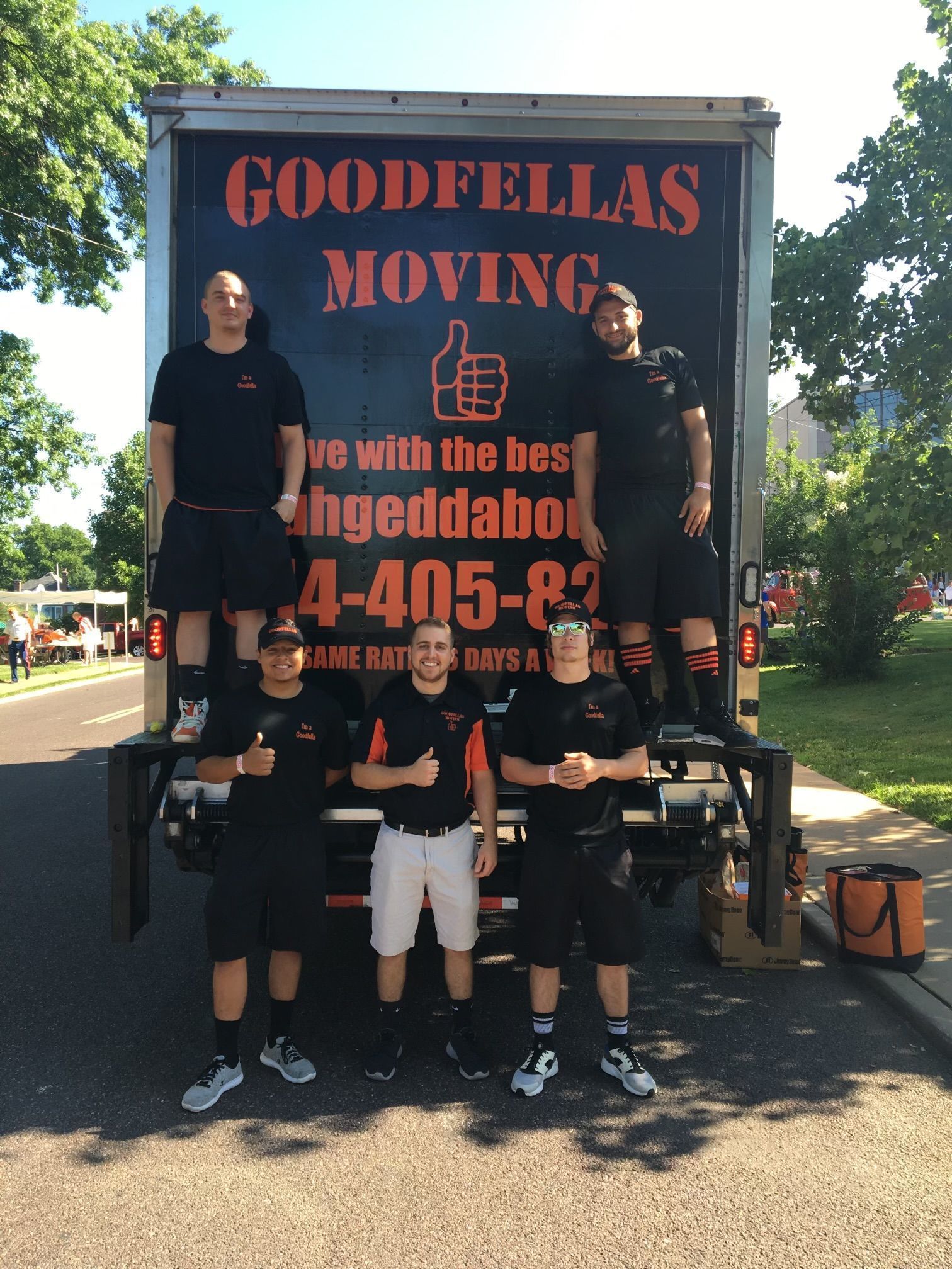 Four movers standing before a Goodfellas Moving truck on a sunny street