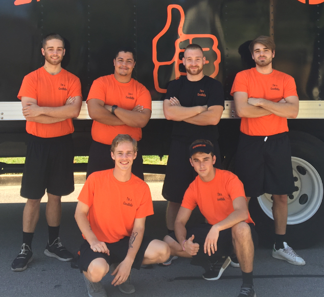 Five people in orange shirts pose in front of a black truck with a neon logo.
