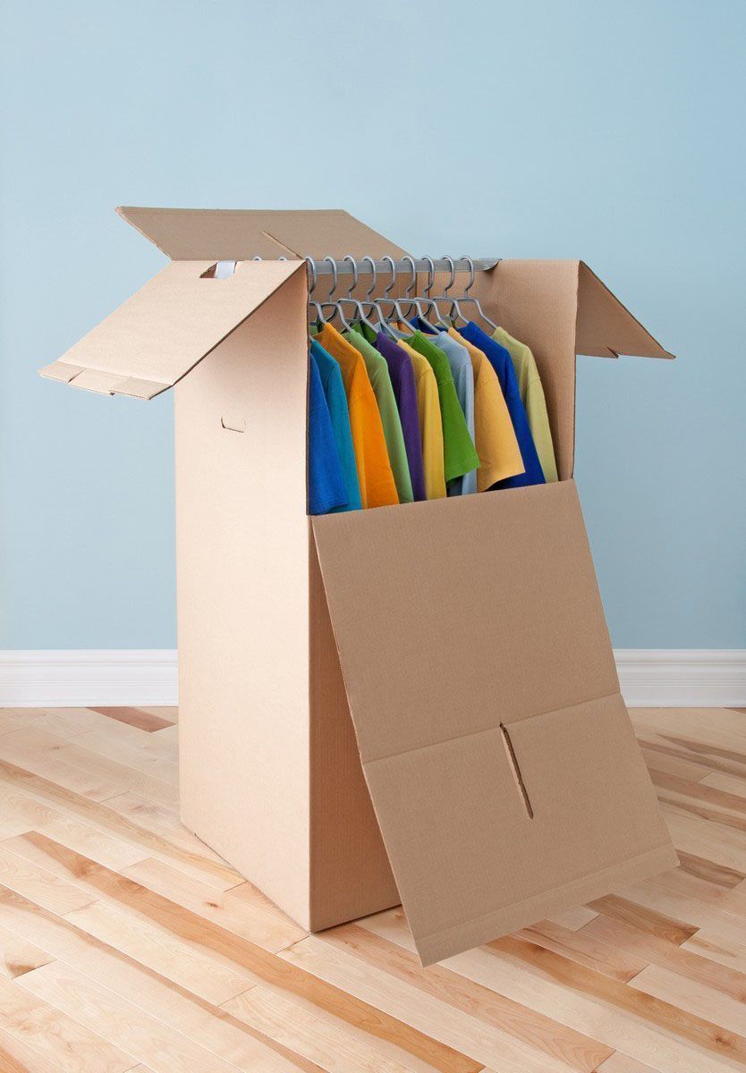 Open cardboard box with colorful shirts hanging inside on a wooden floor