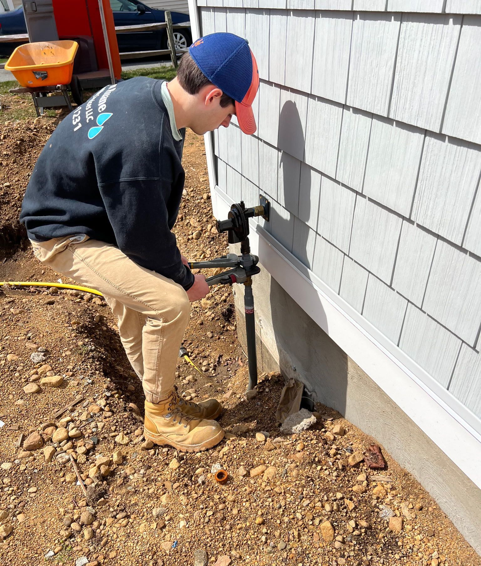 Person in work clothes using a tool near a building's foundation.