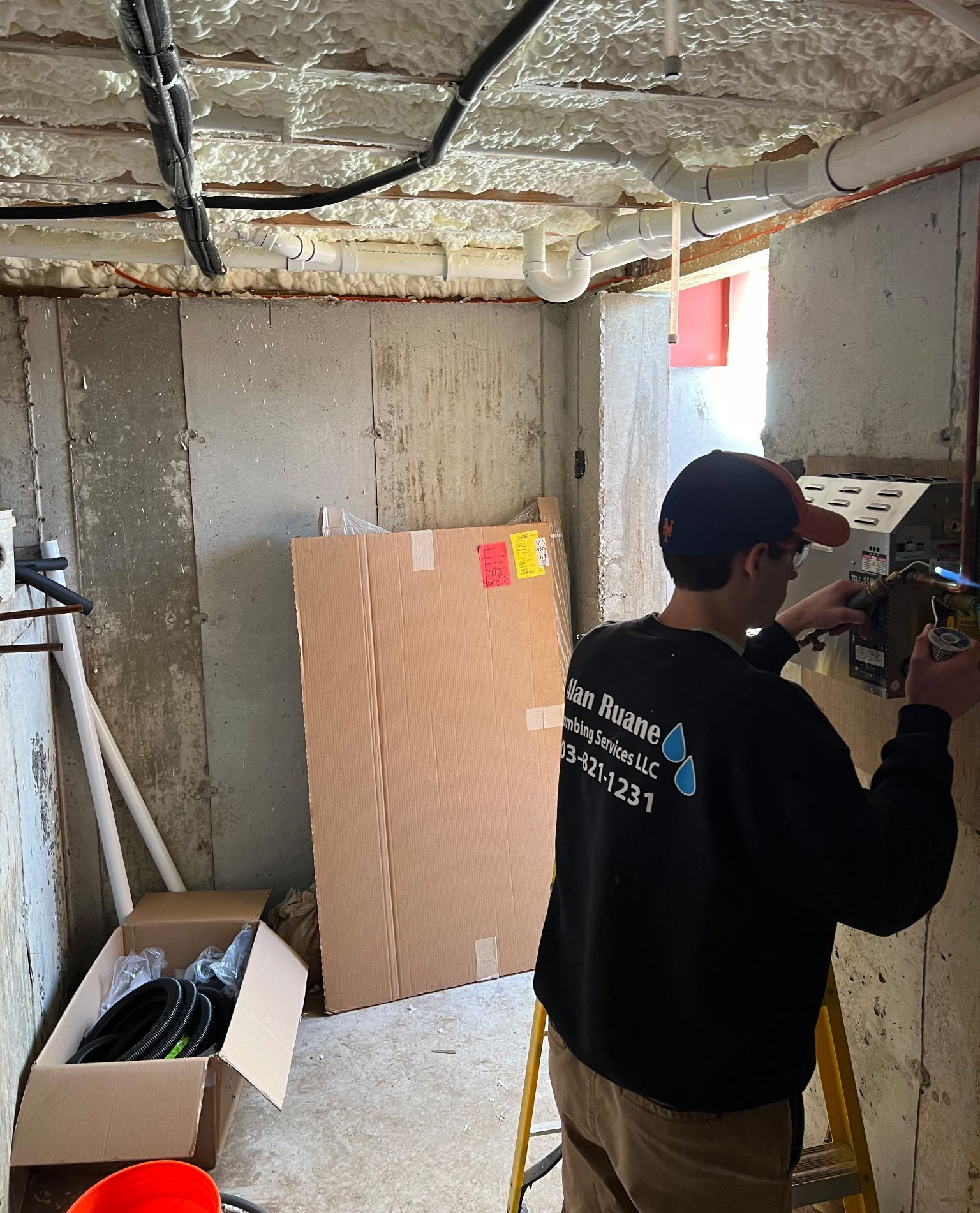 Plumber working on equipment in a basement. Cardboard box and tools nearby.