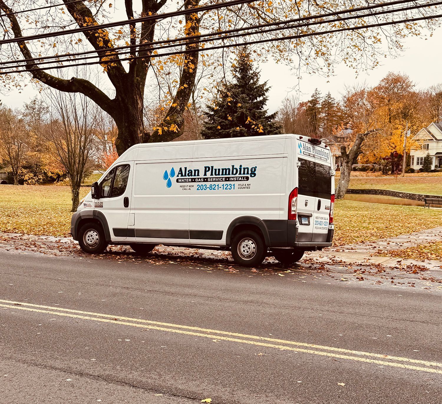 White Alan Plumbing van parked on a street with fall foliage.
