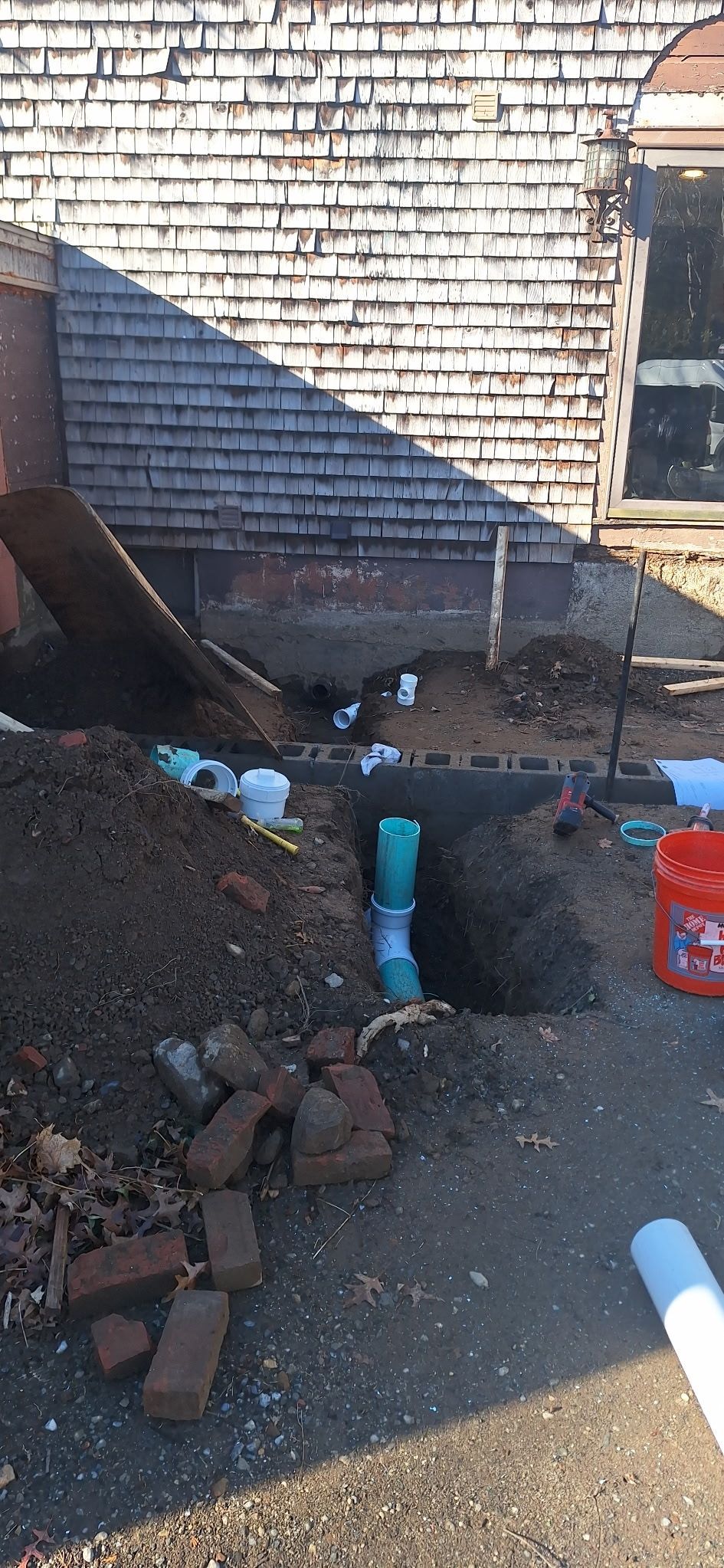 Plumbing work on a construction site. Pipes, dirt, bricks, and a building are visible.