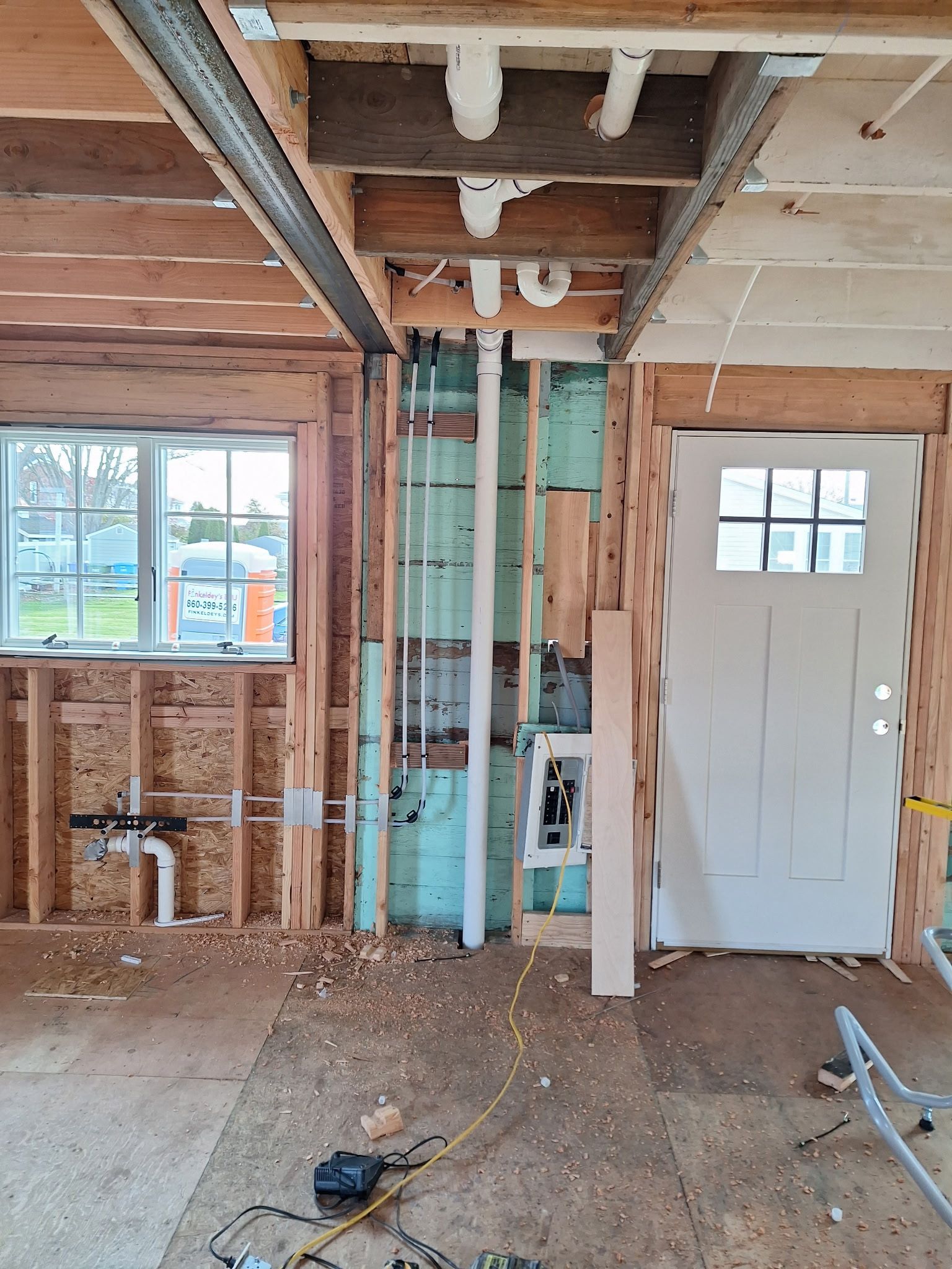 Interior construction: exposed framing, plumbing, window, door, insulation, ceiling pipes, and tools on the floor.