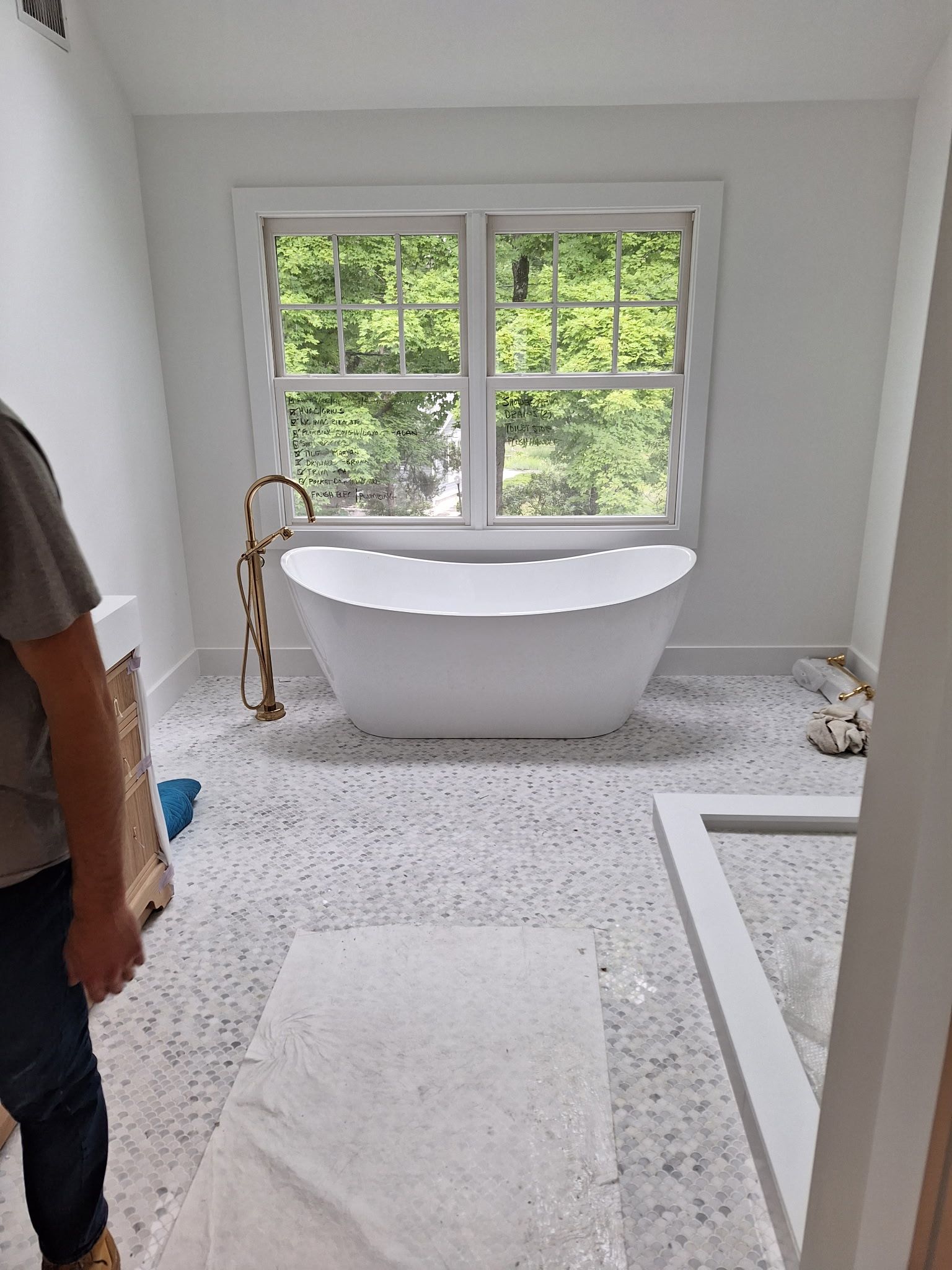 Bathroom with white bathtub, window, and person standing.