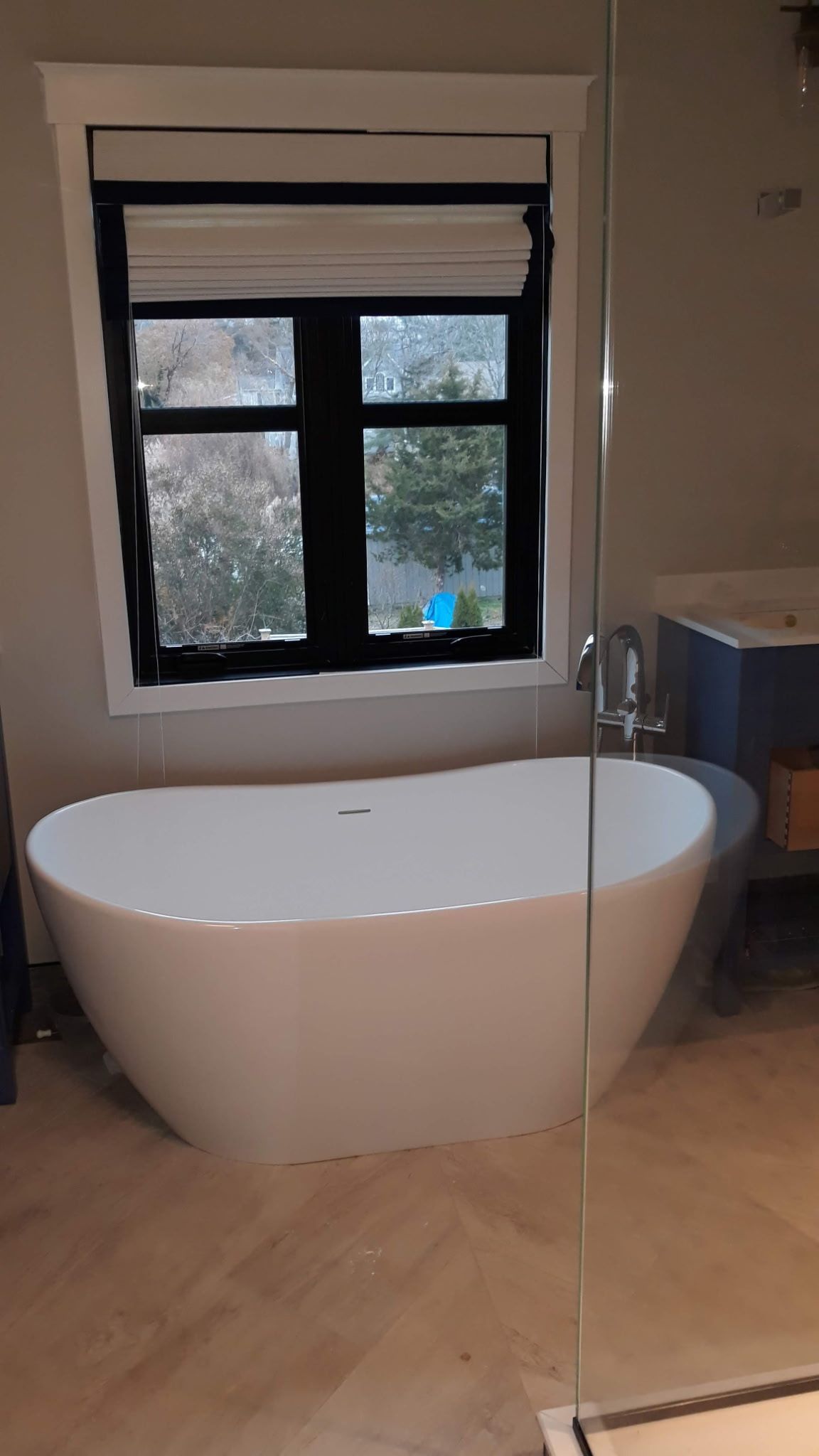 Modern bathroom with white freestanding tub under a window with black trim and a glass shower.
