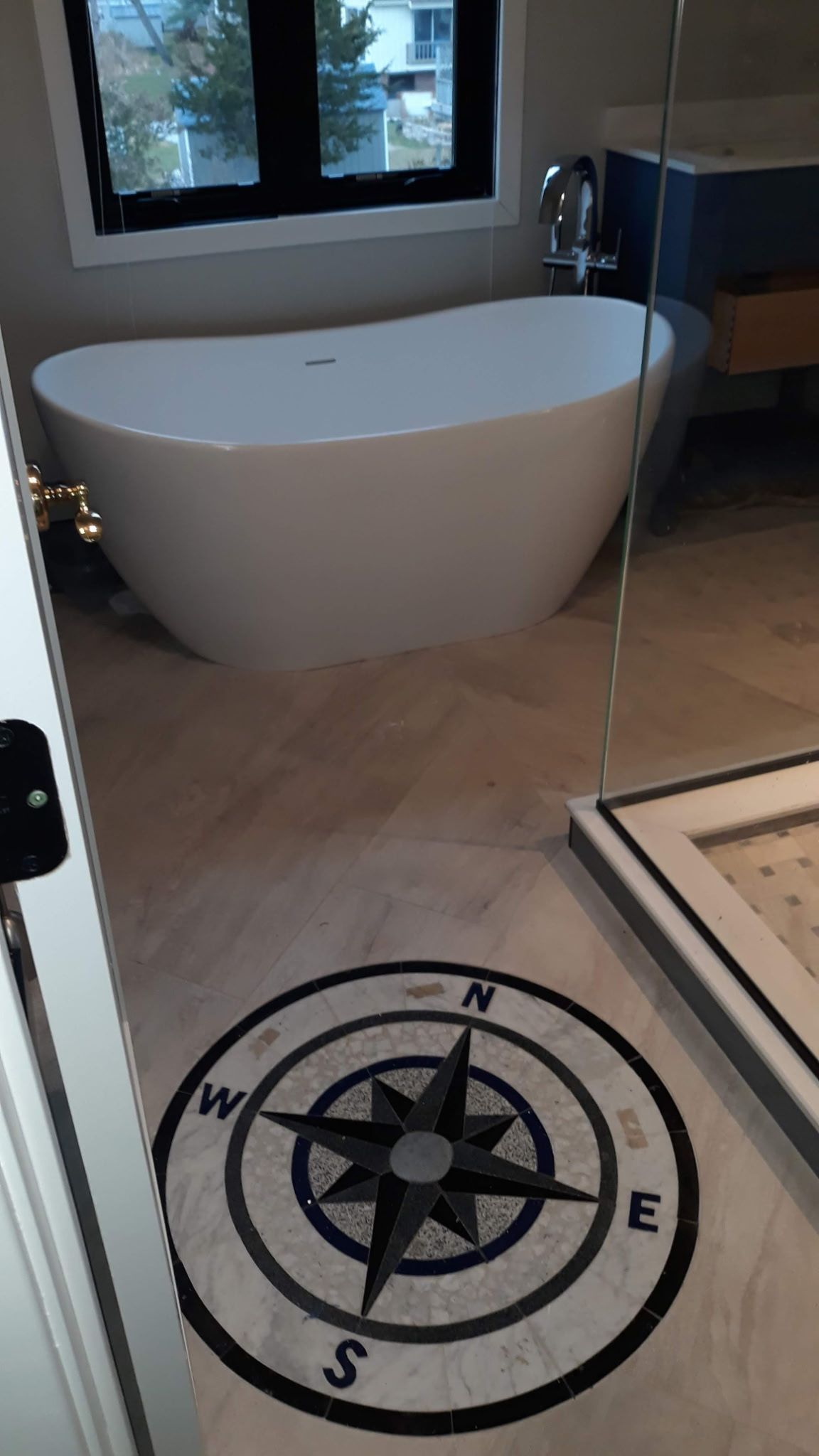 Bathroom with a white tub, window, and a compass rose mosaic tile on the floor.