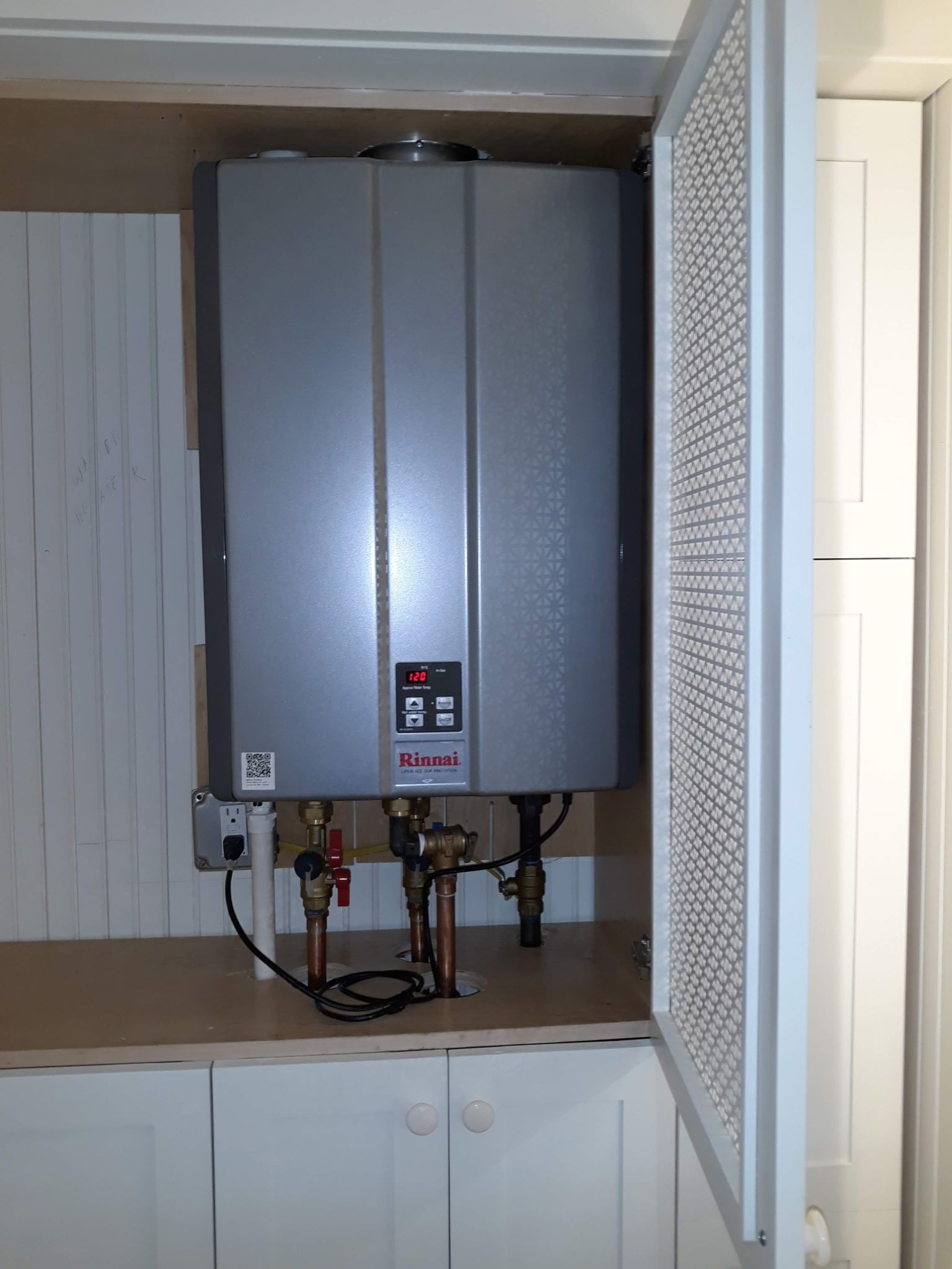Tankless water heater installed in a white cabinet with door open, copper pipes and digital display.