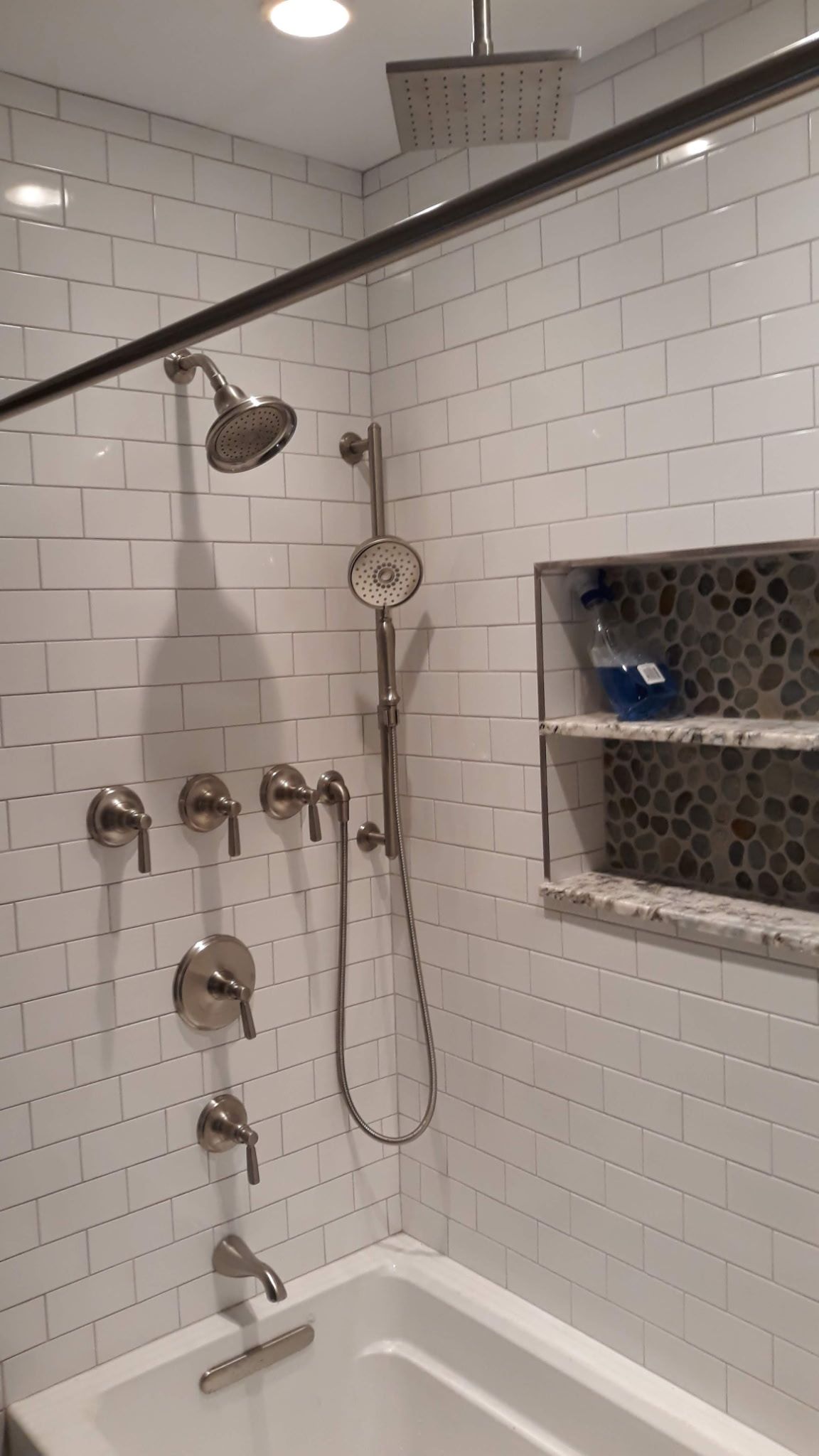 Bathroom with white subway tile, multiple shower heads, and built-in shelf.