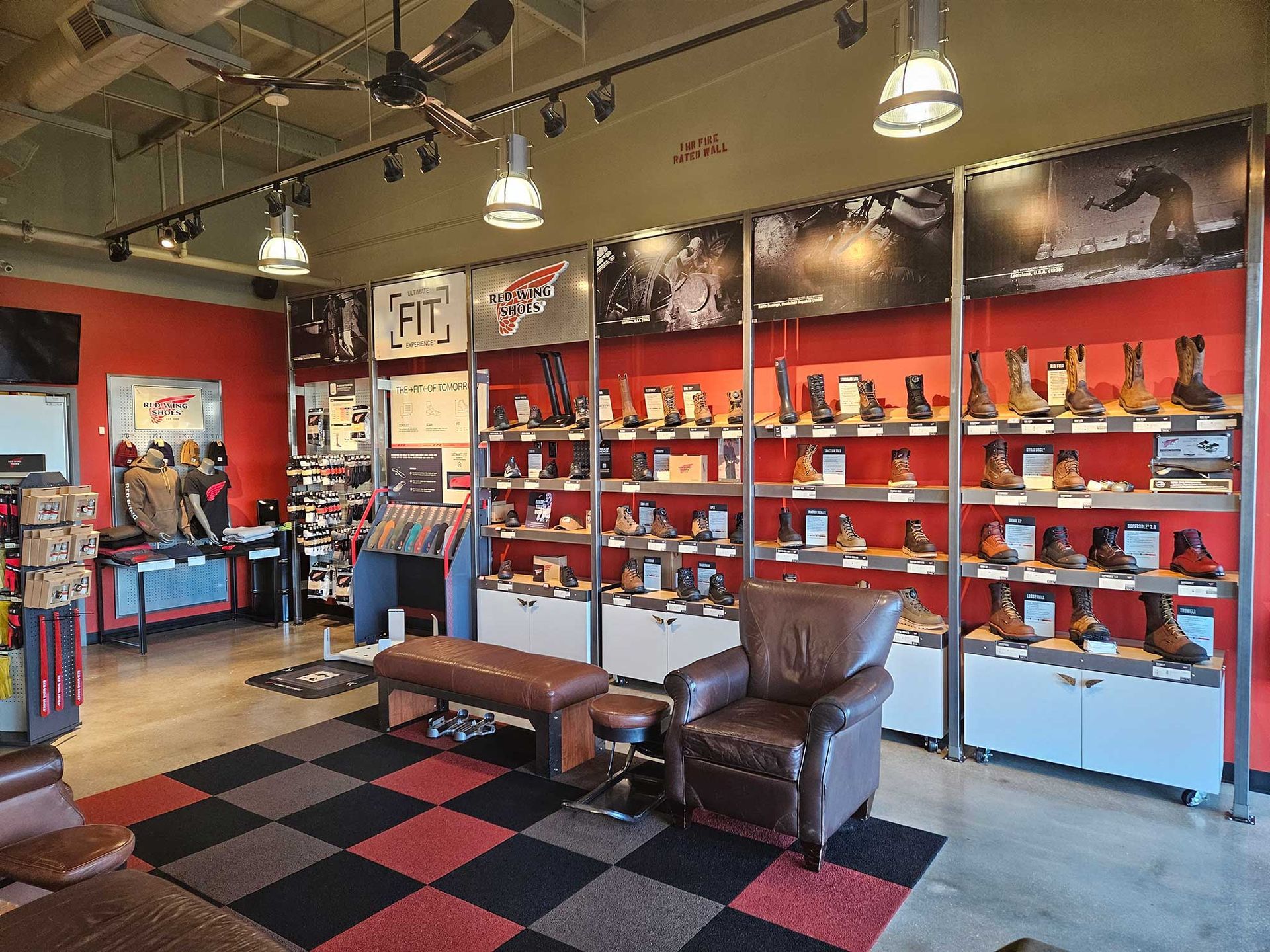 Interior of a boot store with rows of boots on shelves. Red walls, black and red checkered floor, seating area.