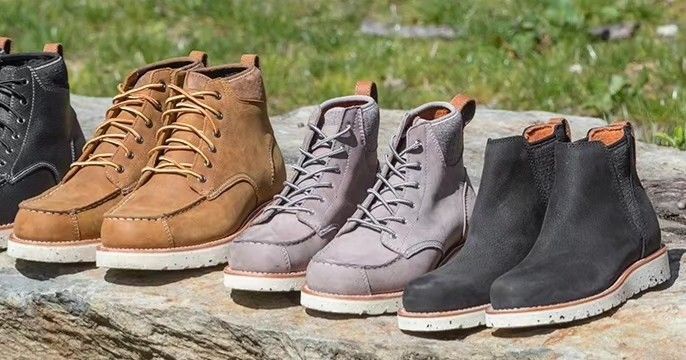 Six pairs of leather boots in various colors, lined up on a stone surface, outdoors.