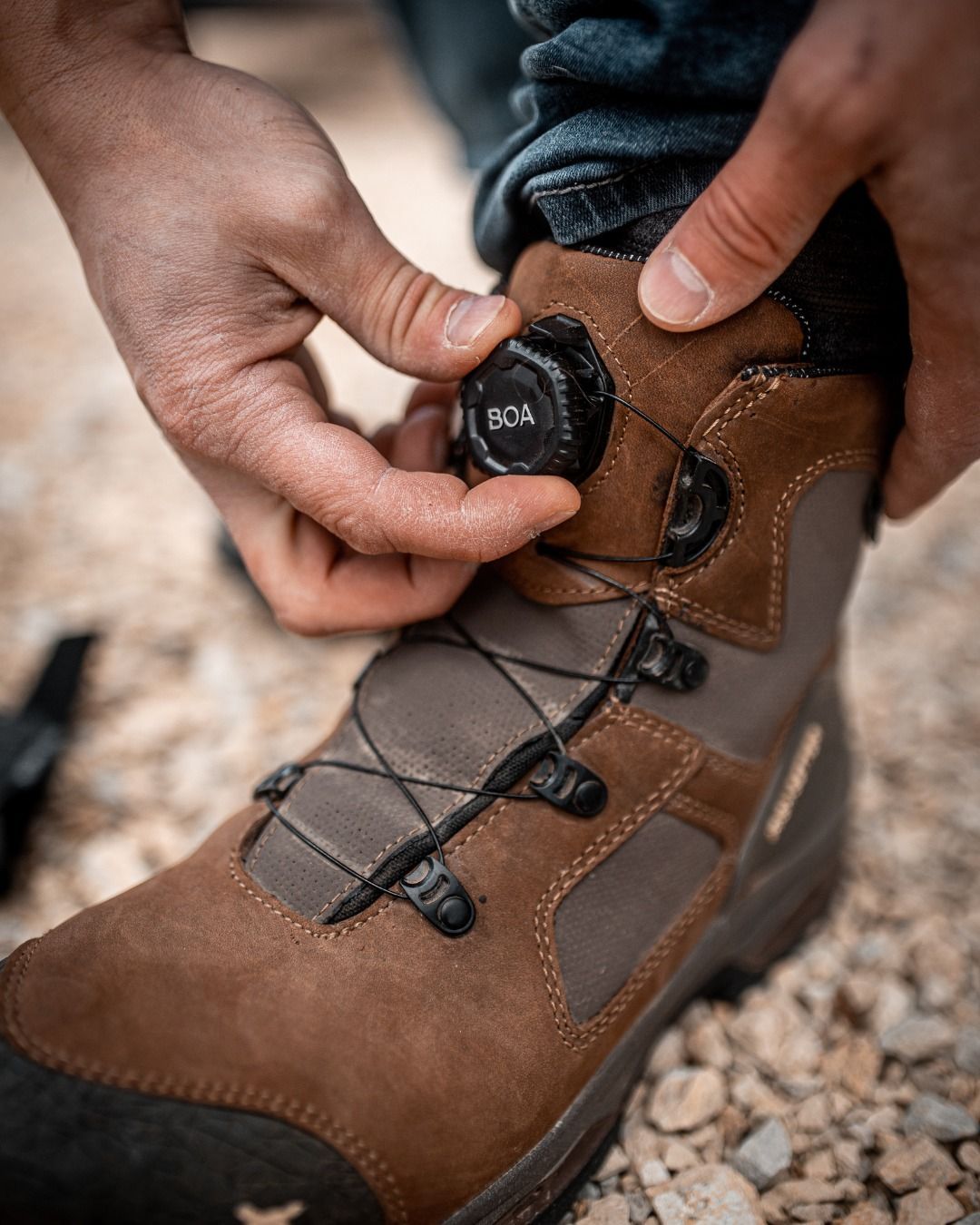 Person adjusting a boot's BOA dial. Brown and gray hiking boot. Hands close-up.