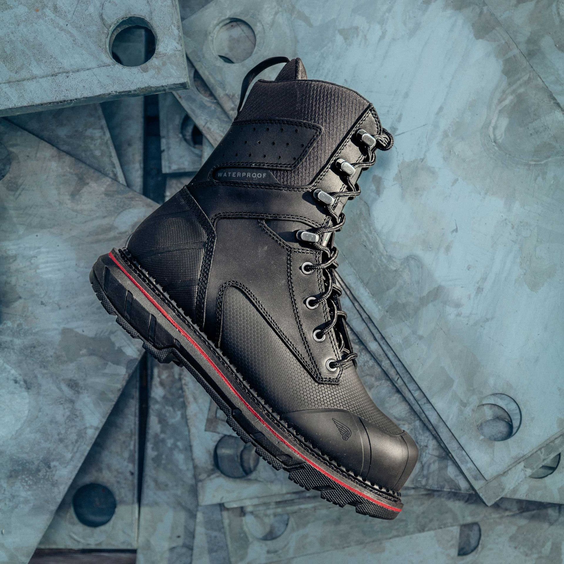 Black work boot, laced, with red accents, set on metal plates.