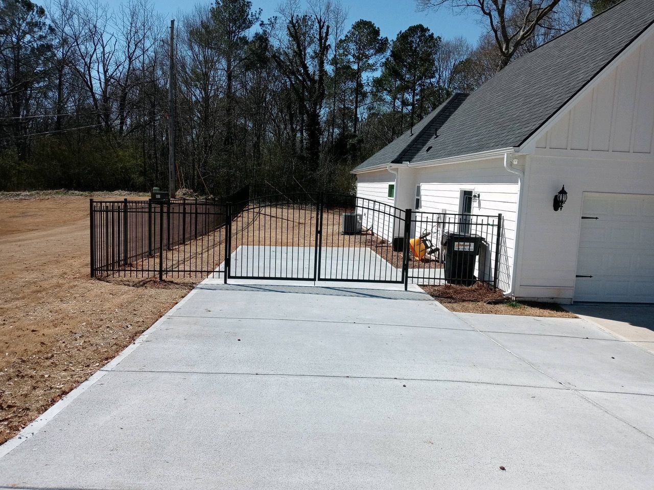 Concrete driveway with a black metal fence leading to a white house with a garage door.