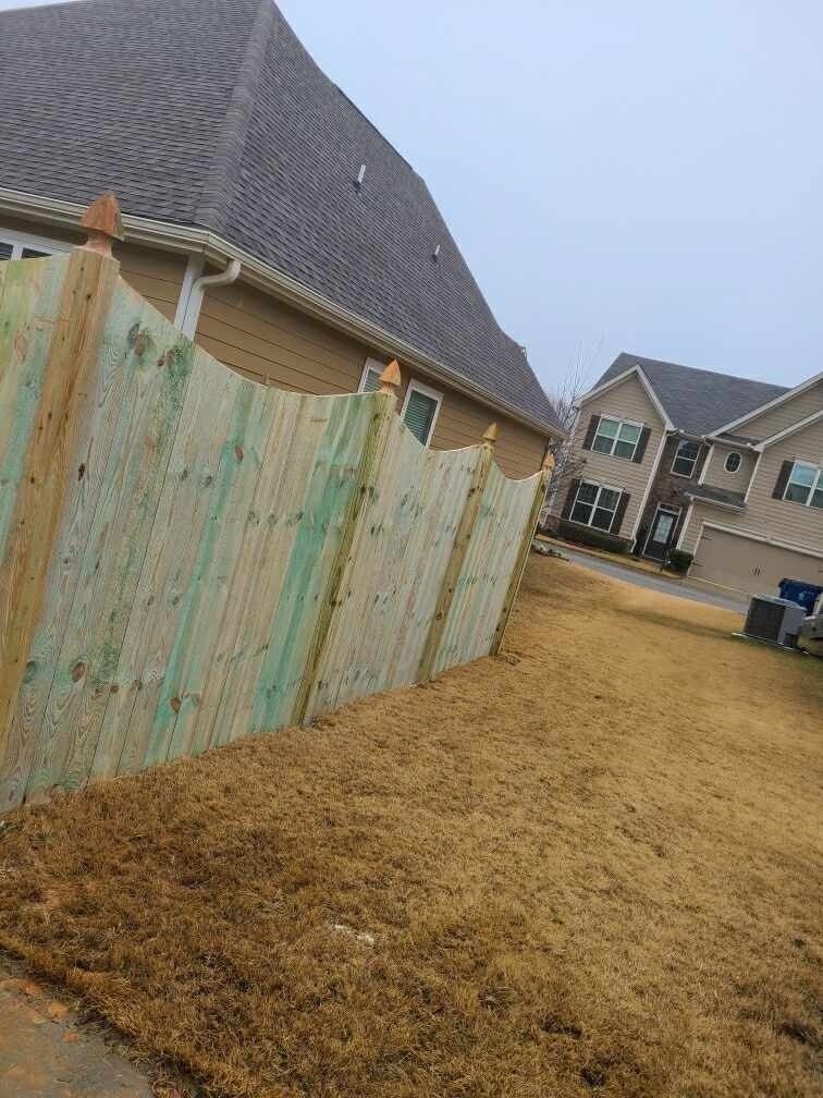 Wooden fence alongside a house and yard on a cloudy day.
