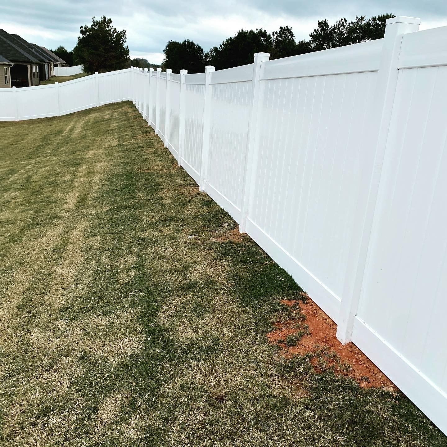 White vinyl fence in a yard with grass and a cloudy sky.