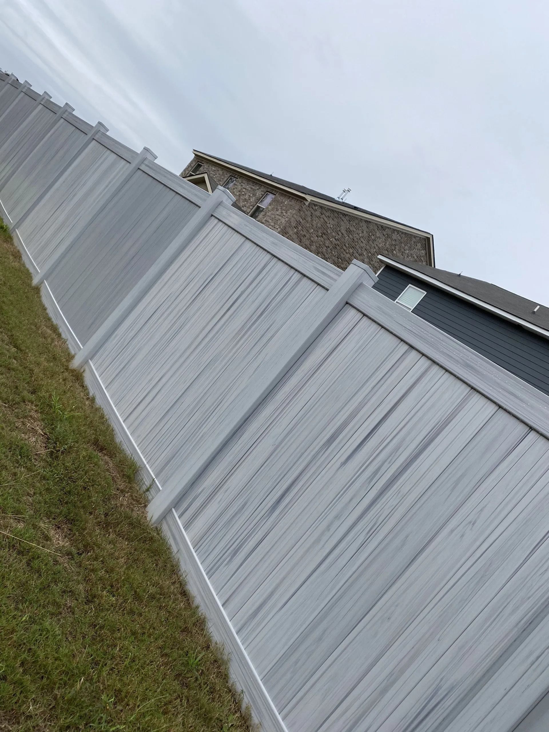Gray vinyl fence along grassy lawn with parts of a house visible.