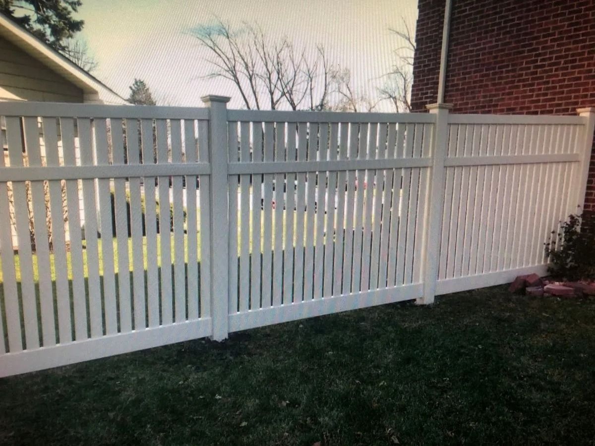 White picket fence in a yard, adjacent to a brick wall.