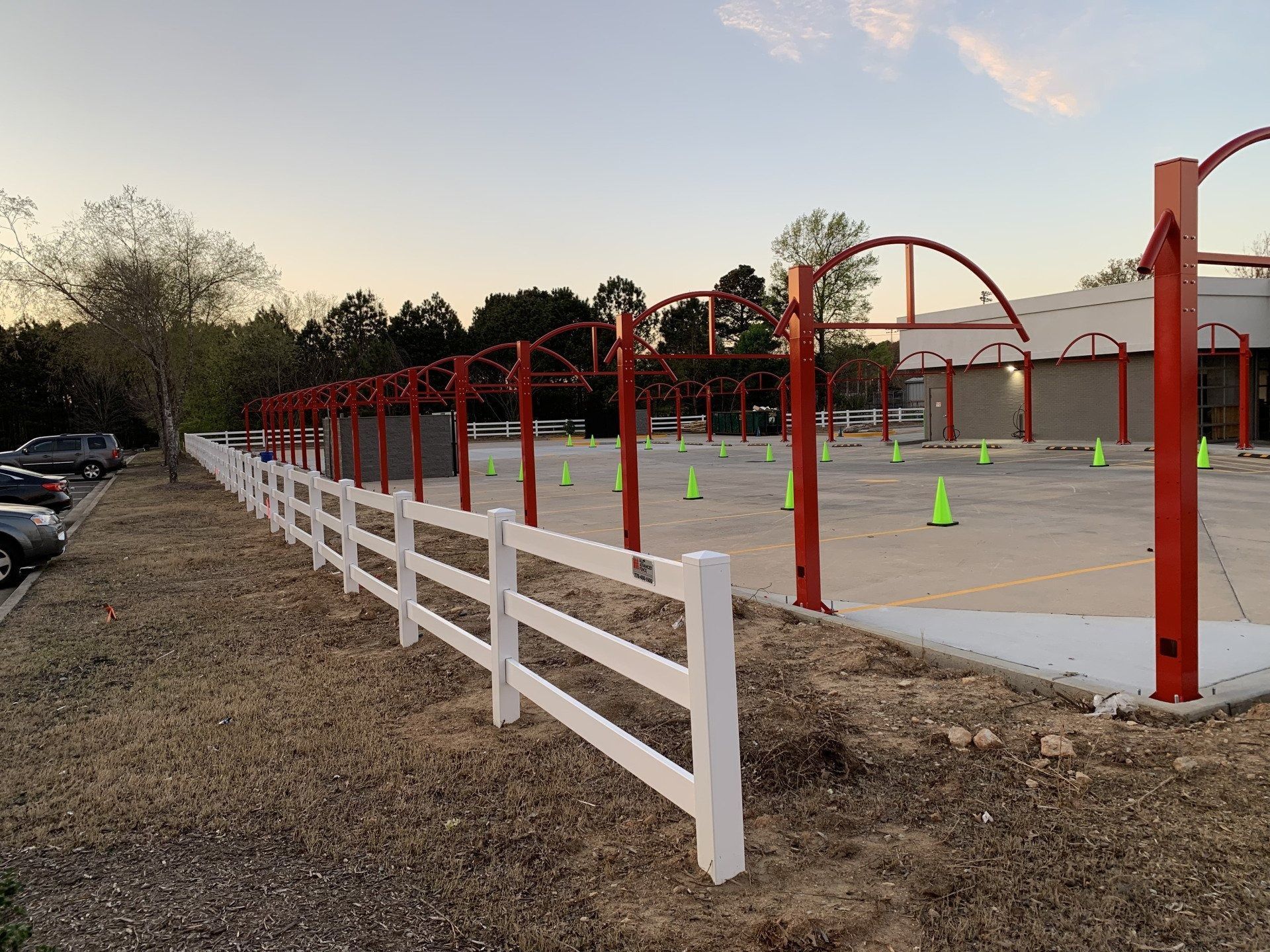 White fence lines a parking lot with red carwash arches and orange cones.