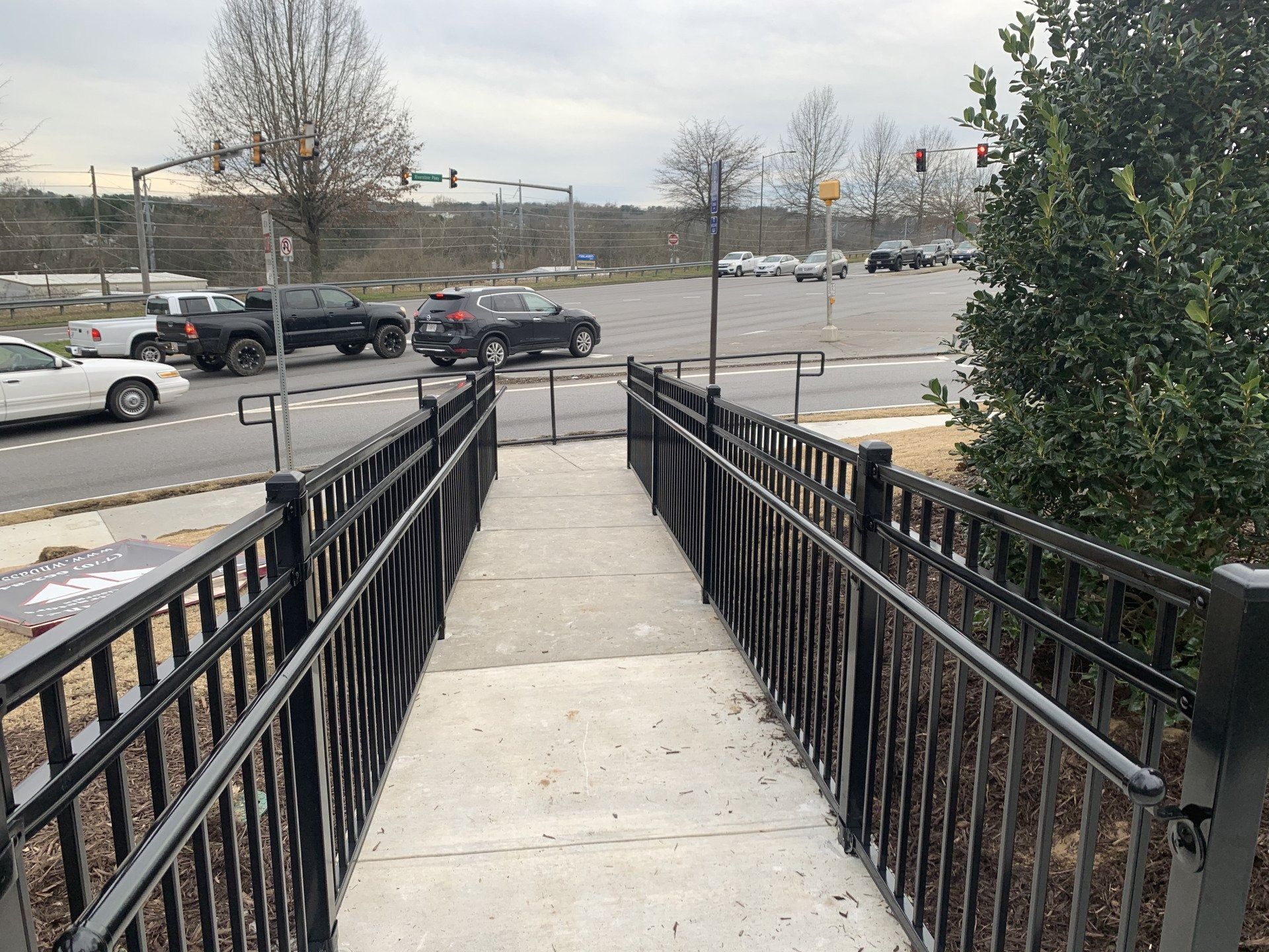 A concrete ramp with black railings leading to a street with cars and a crosswalk.
