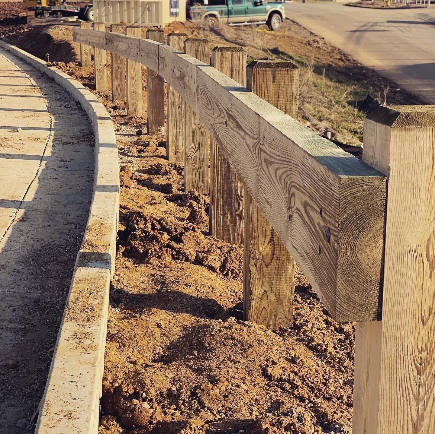 Wooden fence under construction bordering a pathway and roadside.